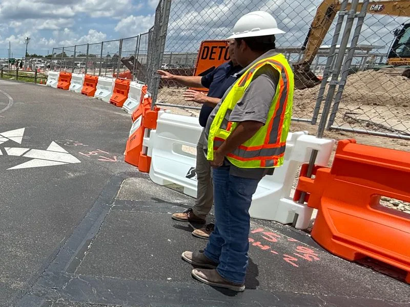 Workers coordinating traffic beside barriers at an airport construction area